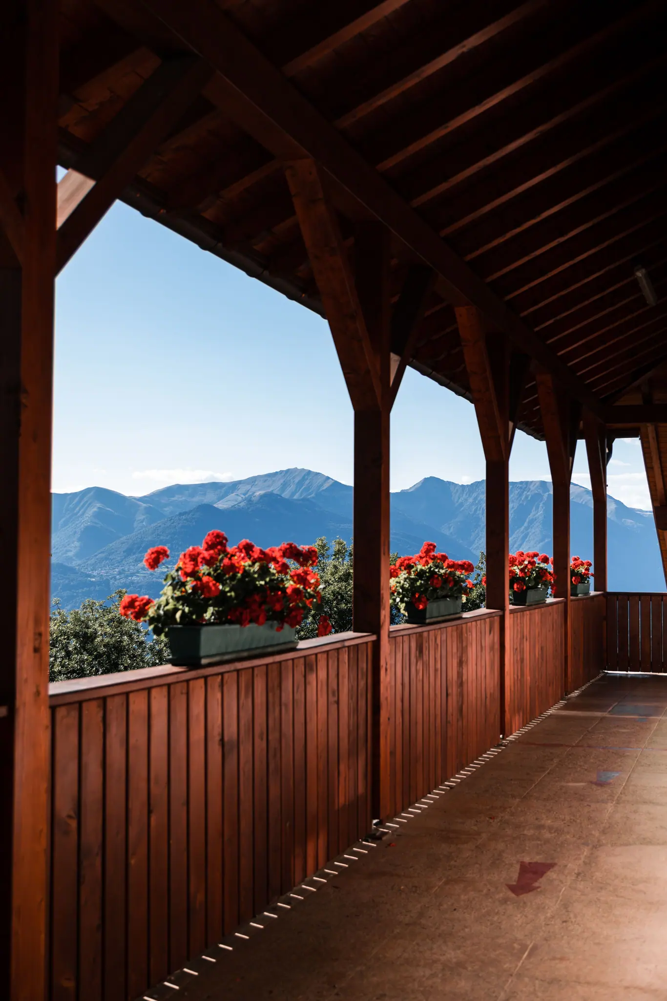 Loggia avec poutres et fermes en bois et jardinières de géraniums rouges, vue sur les montagnes