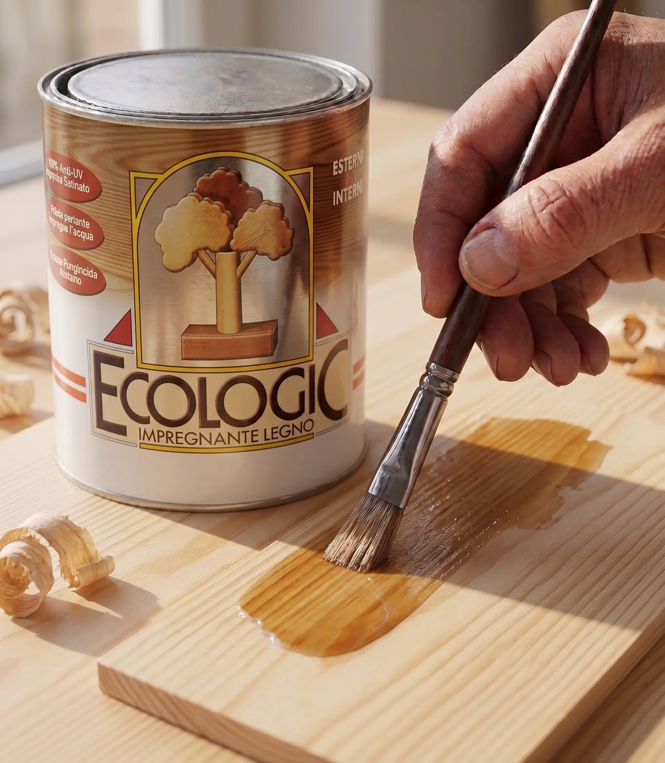 A lata de Ecologic, impregnante para madeira, ao lado de uma mão que aplica o produto a pincel sobre uma tábua clara