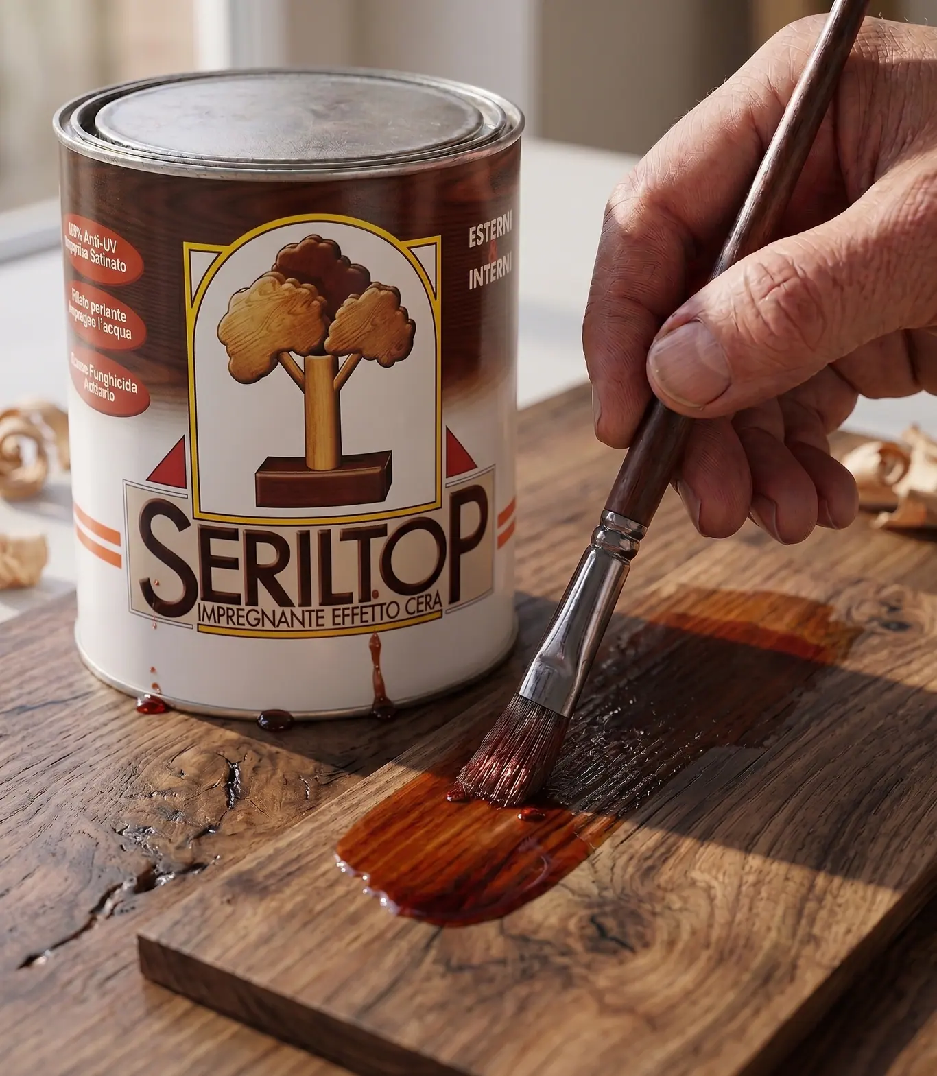 A lata de Seriltop, impregnante efeito cera, ao lado de uma mão que aplica o produto a pincel sobre uma tábua escura