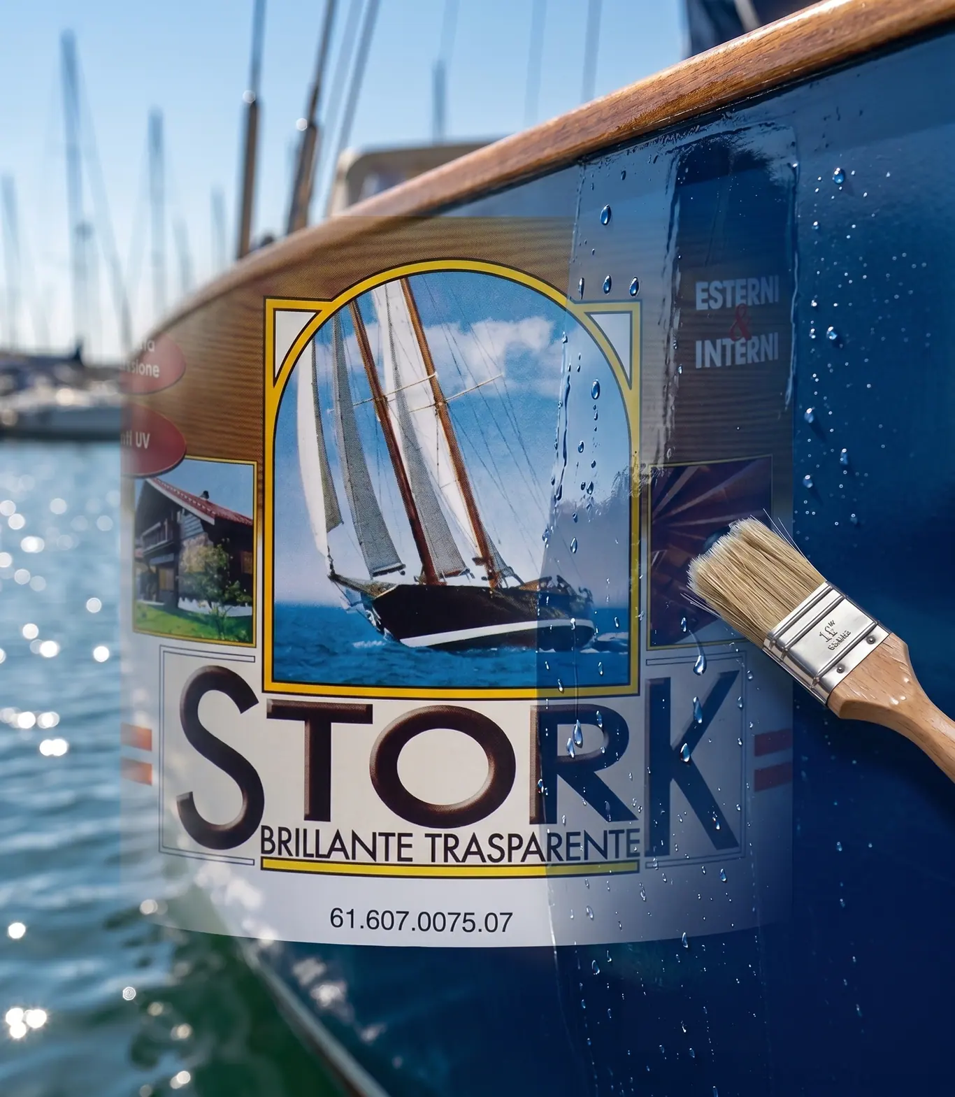 A lata de Stork Brillante Trasparente ao lado de um pincel, em frente ao casco azul de um barco, com os mastros do porto ao fundo