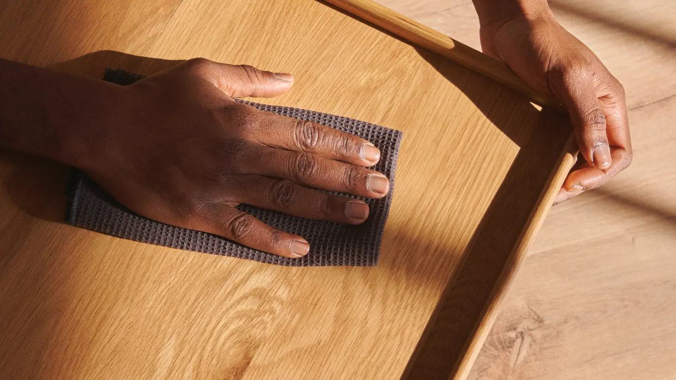 Deux mains poncent avec une cale abrasive le plateau d'une table en chêne clair