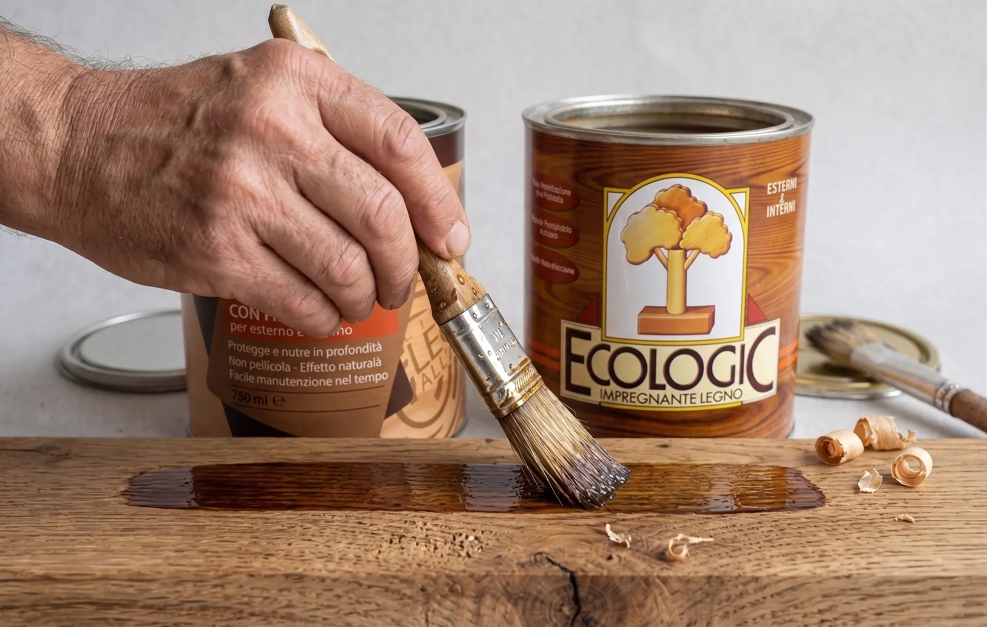 Une main applique le produit au pinceau sur une planche foncée, avec les deux pots comparés en arrière-plan