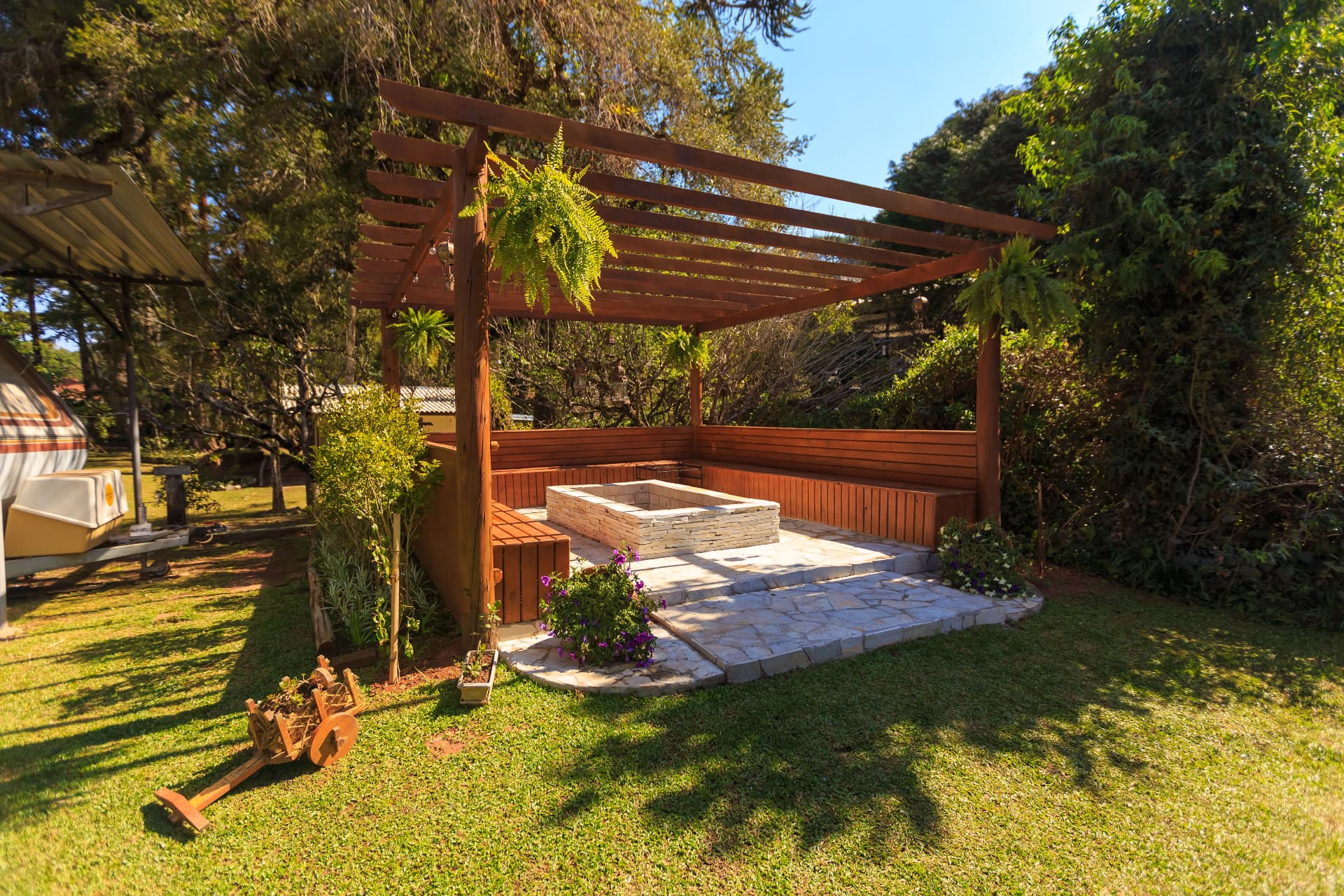 Pergola en bois avec assises et foyer en pierre, dans un jardin