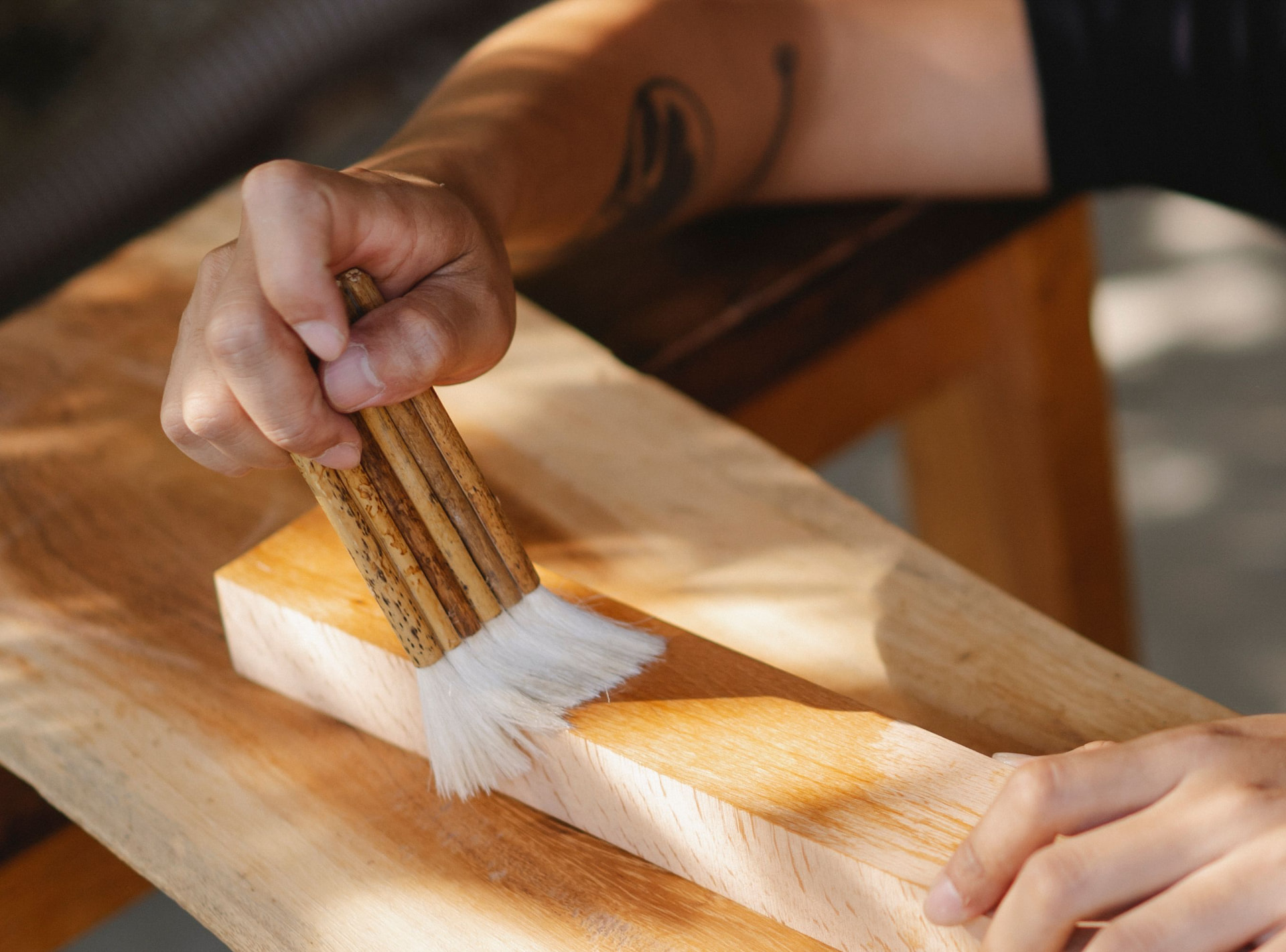 Détail d'une main qui passe un pinceau sur une planche de bois